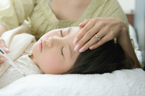 A child resting in bed with a thermometer, showing how parents should focus on overall symptoms and hydration rather than just the fever reading.