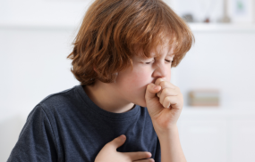 A child clutching his tight chest, while coughing hard, signifying other symptoms, that can sometimes point to an underlying condition that needs assessment.