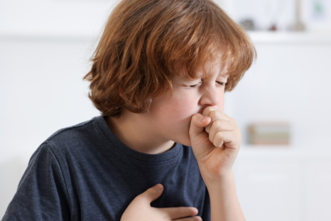 A child clutching his tight chest, while coughing hard, signifying other symptoms, that can sometimes point to an underlying condition that needs assessment.