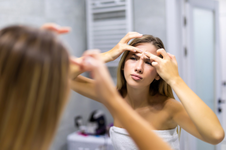 young woman squeezing pimples while looking at the mirror